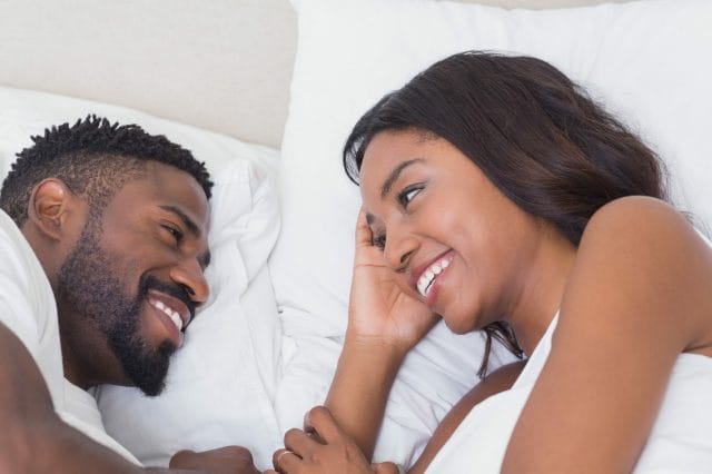 Happy Couple Lying In Bed Together At Home In Bedroom