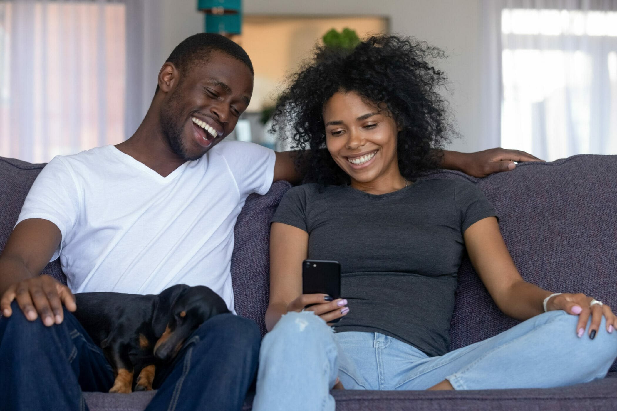 Happy Black African Couple With Pet Laughing Looking At Smartphone